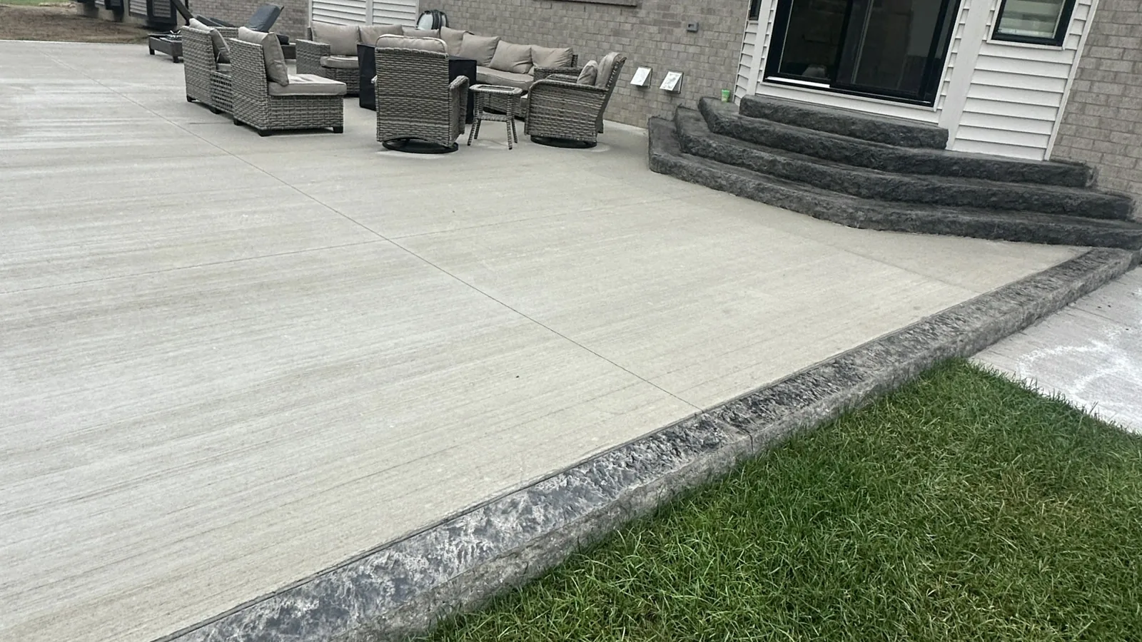A pale concrete patio with a textured charcoal border and curved entry steps