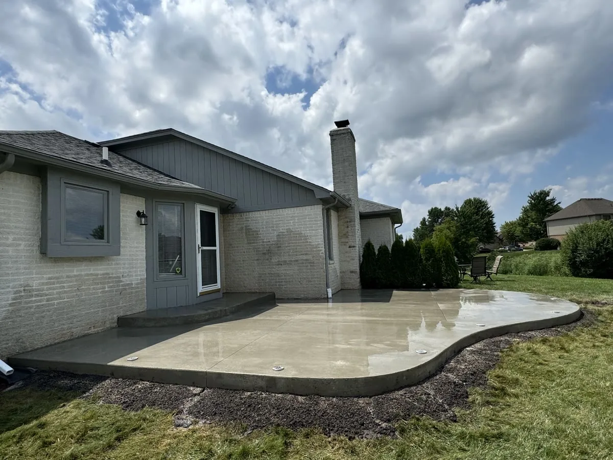 A curved concrete patio and entry step beside a white brick home